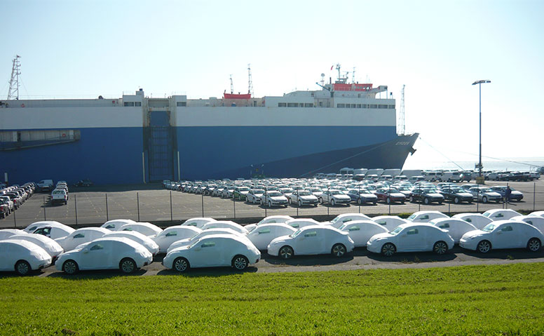 Automobile handling: The loading port in Emden with many new cars in white protective foil and a car carrier in the background