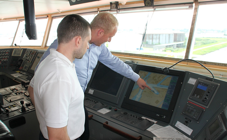 Eine Person erklärt einer anderen Perosn in der Kommandobrücke die Route auf einem Monitor