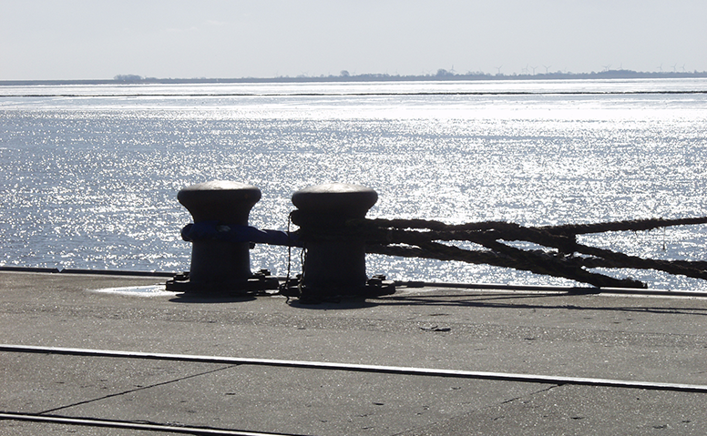 Terminal Emskai: Two bollards on the pier at sunset, with ropes tied to them. The Ems River can be seen in the background