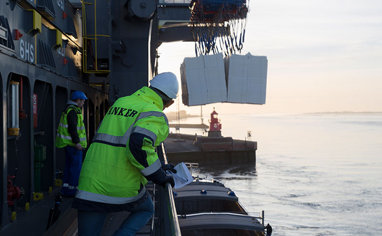 Handling of Forest Products: Two people in yellow Anker Schiffahrt warning jackets are supervising the loading of a cargo ship with forest products
